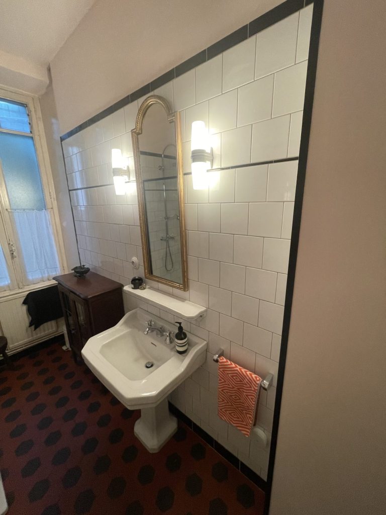Salle de bains : lavabo, miroir et carrelage blanc à frise noire
