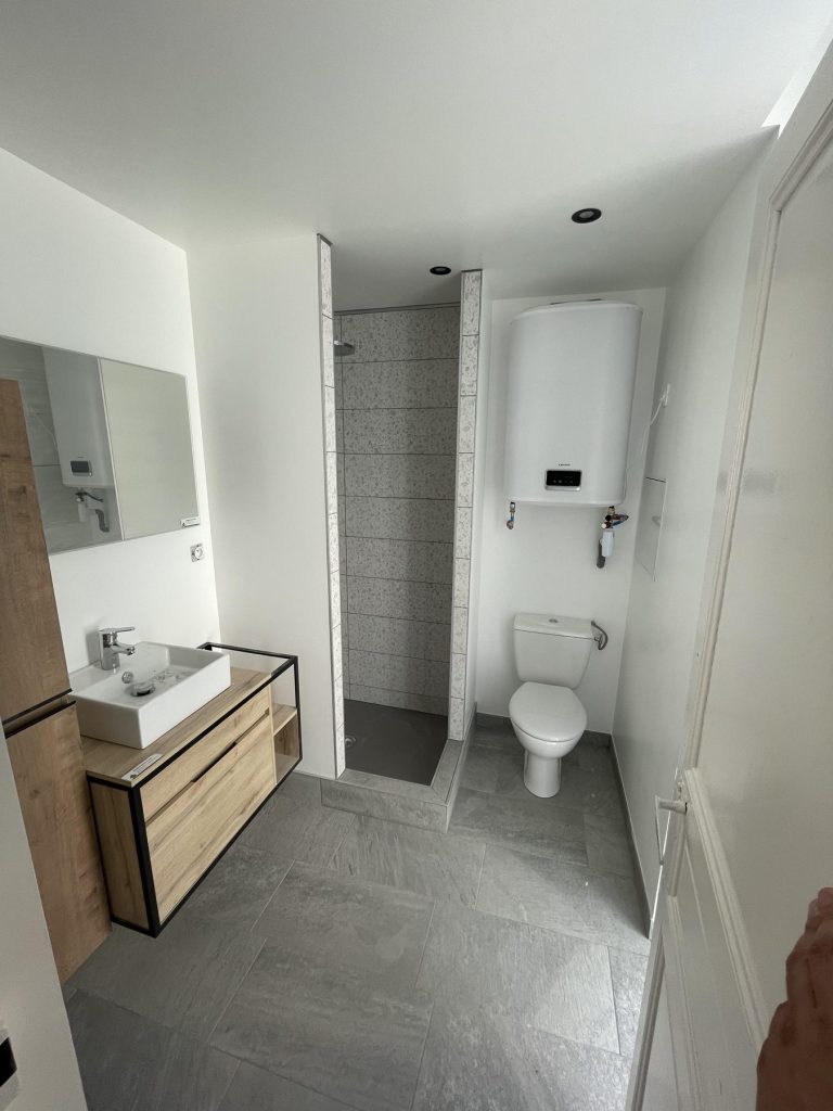 Salle de bains : receveur de douche, carrelage mural effet terrazzo et sol en grands carreaux gris